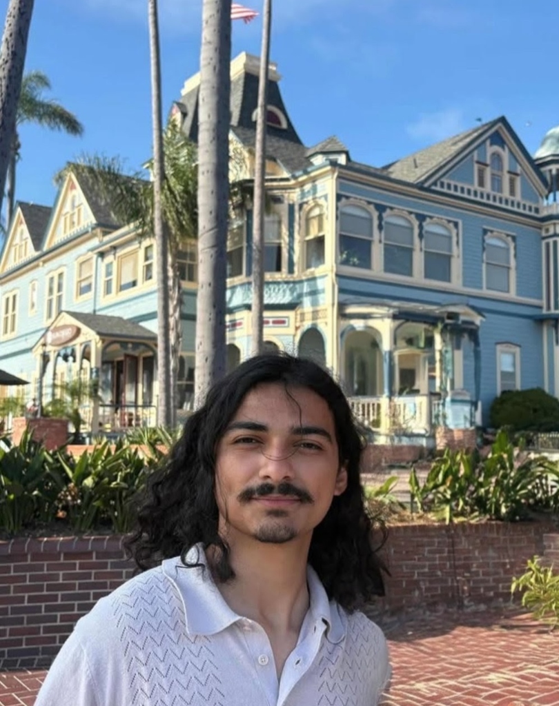 Isaac Portillo standing in front of a blue Victorian house